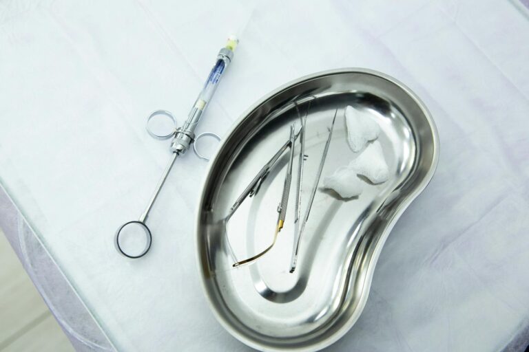 A set of sterile medical tools and syringe displayed in a kidney tray for dental or surgical use.