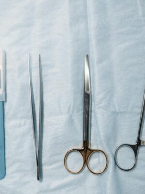 Flat lay of surgical tools including scissors, forceps, and syringe on a sterile blue cloth.