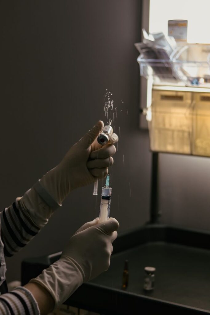 Scientist wearing gloves using a syringe to prepare a solution in a dimly lit laboratory.