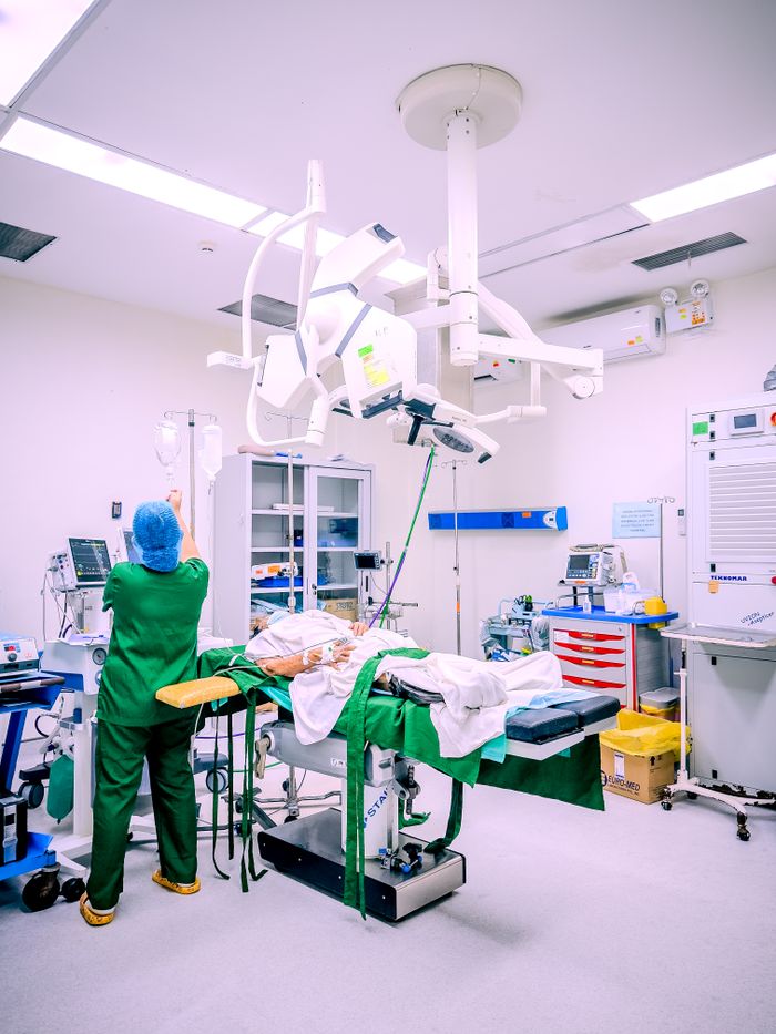 A nurse in a Central Visayas hospital operating room setting adjusting IV equipment during surgery.